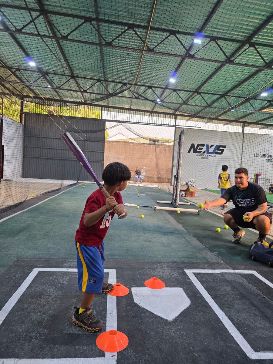 Niño pequeño bateando con entrenador en Nexus Sport Center