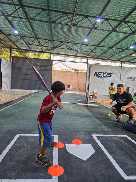 Niño pequeño bateando con entrenador en Nexus Sport Center