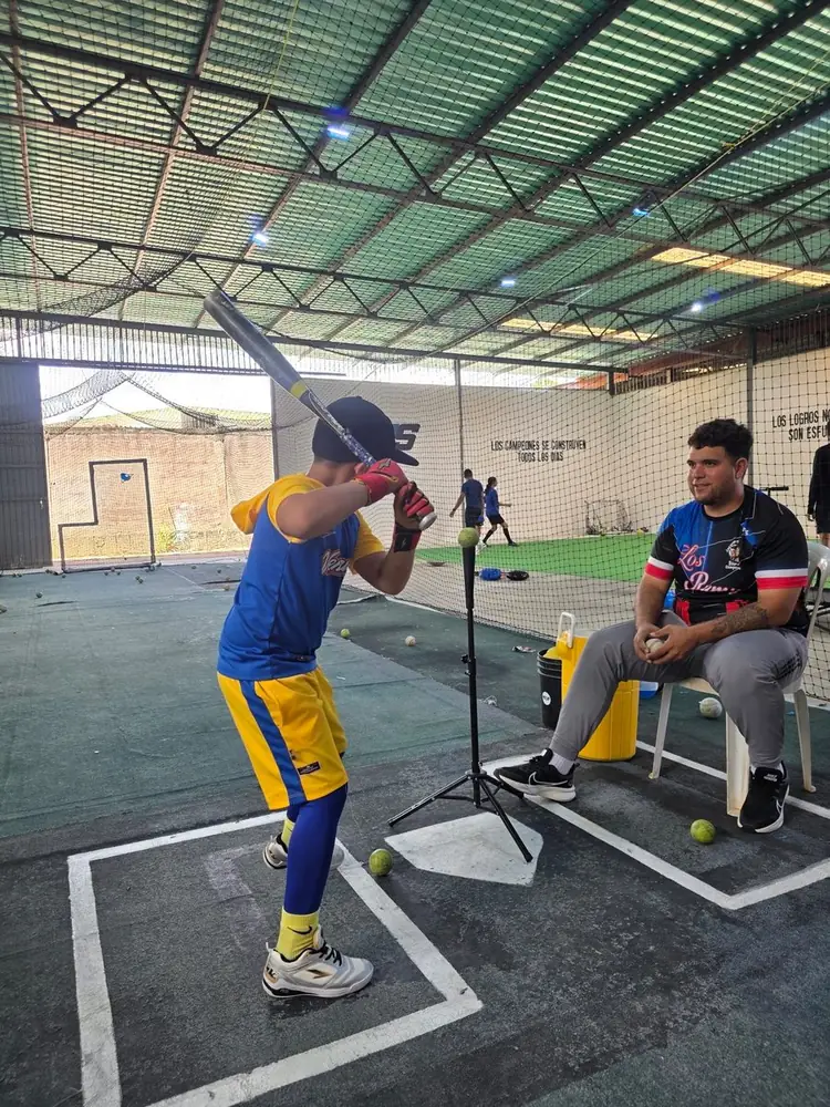 Niño practicando bateo con entrenador en la jaula de Nexus Sport Center